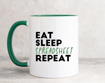 May include: White ceramic mug with a green rim and handle. The mug has black text that reads "Eat Sleep Spreadsheet Repeat" with the word "Spreadsheet" in green.