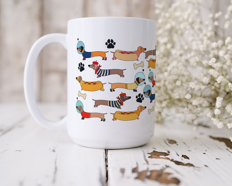 May include: White ceramic coffee mug with a colorful illustration of dachshunds wearing different costumes and accessories, including astronaut helmets, hot dog costumes, and roller skates.