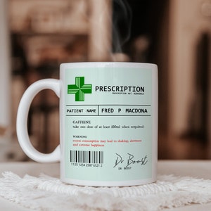 May include: White ceramic coffee mug with a green cross and the text "PRESCRIPTION" printed on it. The mug also has the text "PATIENT NAME FRED P MACDONA" and "CAFFEINE take one dose of at least 250ml when required". The mug has a warning that says "excess consumption may lead to shaking, alertness and extreme happiness". The mug also has a barcode and the text "Dr Boost" with the text "DR BOOST" underneath.