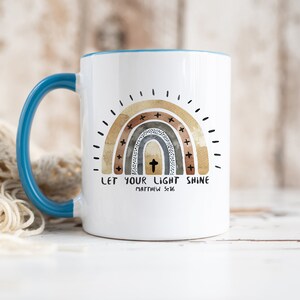 May include: White ceramic mug with a teal rim and handle. The mug features a watercolour rainbow with a cross in the centre and the text "Let your light shine Matthew 5:16".