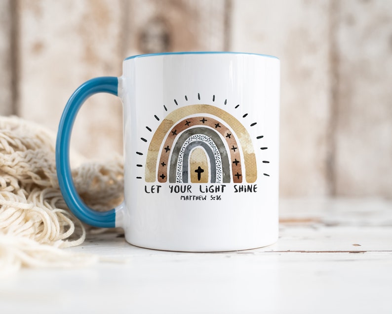 May include: White ceramic mug with a teal rim and handle. The mug features a watercolour rainbow with a cross in the centre and the text "Let your light shine Matthew 5:16".