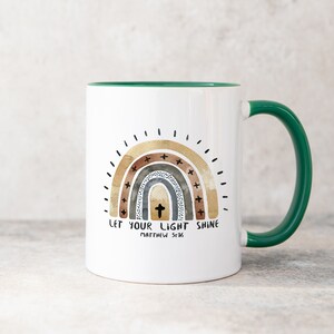 May include: White ceramic mug with a green rim and handle. The mug features a rainbow design with a cross in the centre and the text "Let your light shine Matthew 5:16".