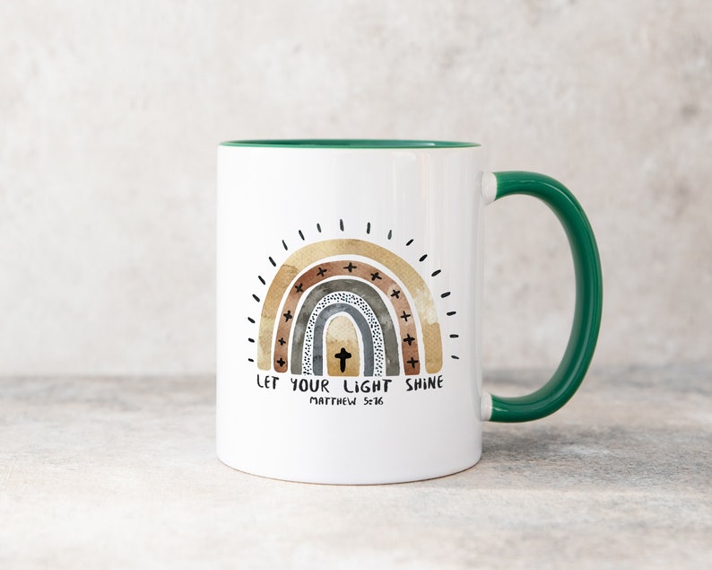 May include: White ceramic mug with a green rim and handle. The mug features a rainbow design with a cross in the centre and the text "Let your light shine Matthew 5:16".