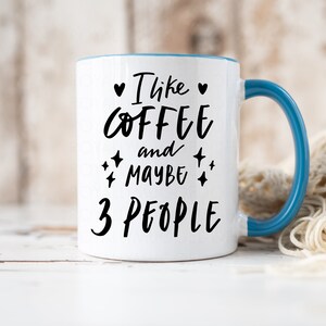 May include: White ceramic mug with a blue rim and handle. The mug has black text that reads "I like coffee and maybe 3 people" with a heart and stars.
