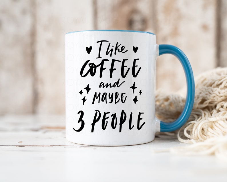 May include: White ceramic mug with a blue rim and handle. The mug has black text that reads "I like coffee and maybe 3 people" with a heart and stars.