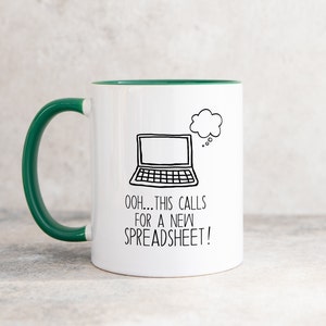 May include: White coffee mug with a green rim and handle. The mug features a black and white illustration of a laptop with a thought bubble above it. The text on the mug reads "Ooh... this calls for a new spreadsheet!"