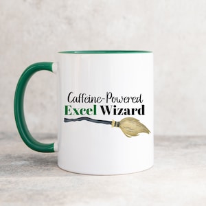 Puede incluir: Taza de cerámica blanca con borde y asa verdes. La taza tiene un gráfico negro y verde de una escoba con el texto "Caffeine-Powered Excel Wizard".