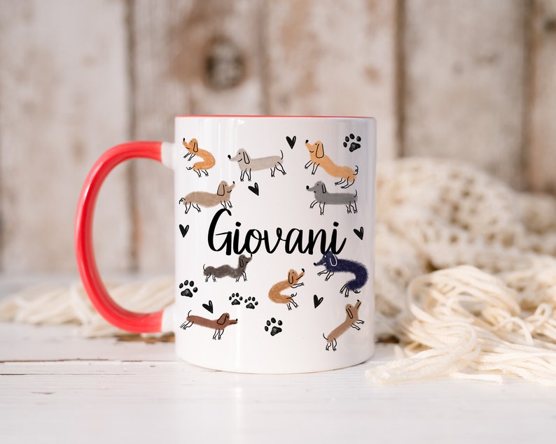 Pode incluir: Uma caneca de cer&acirc;mica branca com uma pega e rebordo interior vermelho brilhante. O exterior apresenta um padr&atilde;o repetitivo de pequenos c&atilde;es dachshund desenhados &agrave; m&atilde;o em v&aacute;rios tons de castanho, cinzento e preto, intercalados com cora&ccedil;&otilde;es e pegadas pretas. O nome Giovani est&aacute; impresso em letra cursiva preta no centro.