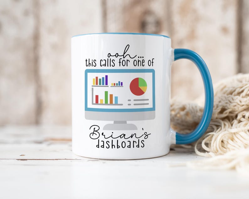 May include: A white ceramic mug with a blue handle and interior rim. The front features a graphic of a computer monitor displaying colorful bar and pie charts. The text reads: ooh... this calls for one of Brian's dashboards in black font.