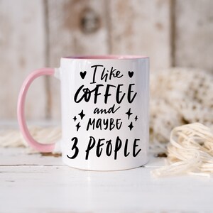 May include: White ceramic mug with a pink rim and handle. The mug has black text that reads "I like coffee and maybe 3 people" with a heart and stars.