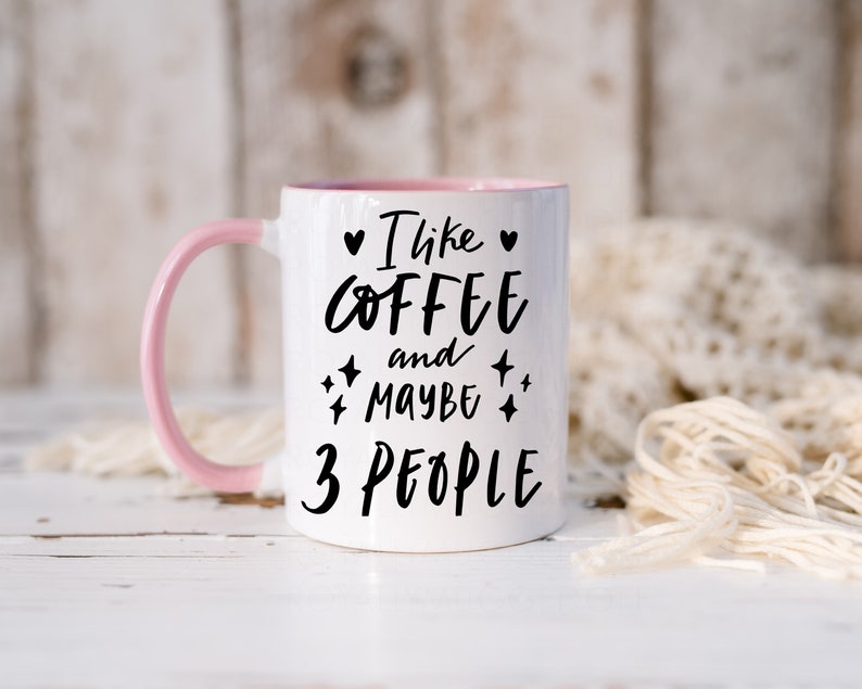 May include: White ceramic mug with a pink rim and handle. The mug has black text that reads "I like coffee and maybe 3 people" with a heart and stars.