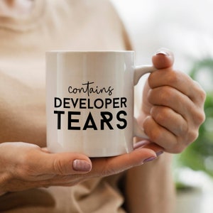 Peut inclure: Une tasse en c&eacute;ramique blanche avec du texte noir qui dit "contient DES LARMES DE D&Eacute;VELOPPEUR".