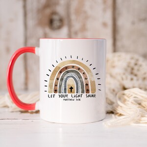 May include: White ceramic coffee mug with a red handle. The mug features a rainbow design with a cross in the centre and the text "Let your light shine Matthew 5:16".