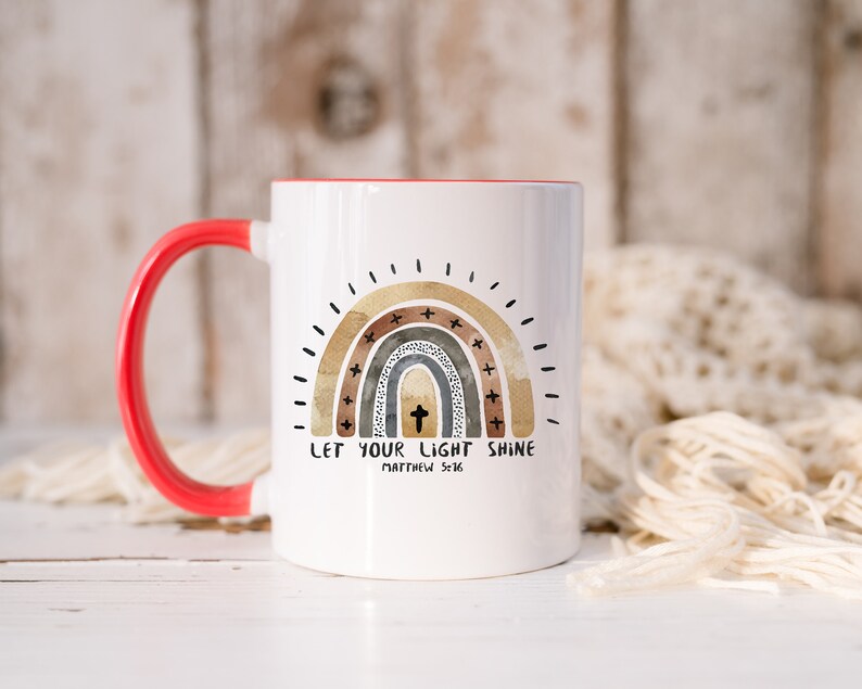 May include: White ceramic coffee mug with a red handle. The mug features a rainbow design with a cross in the centre and the text "Let your light shine Matthew 5:16".
