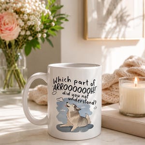 May include: A white ceramic mug featuring a graphic of a howling husky dog and the black text: Which part of ARROOOOOOH! did you not understand? The mug has a curved handle and a smooth finish, displaying a clear illustration of the dog.