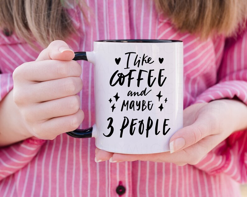 May include: White coffee mug with a black rim and handle. The mug has black text that reads "I like coffee and maybe 3 people" with hearts and stars around the text.