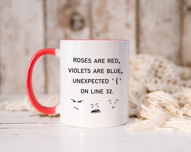 Może przedstawiać: Biały ceramiczny kubek do kawy z czerwonym uchwytem. Kubek ma czarny wz&oacute;r z tekstem "ROSES ARE RED, VIOLETS ARE BLUE, UNEXPECTED '{' ON LINE 32." i trzy kresk&oacute;wkowe twarze.
