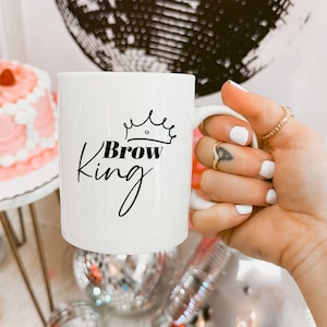 Peut inclure: Une tasse en céramique blanche avec une couronne noire et le texte "Brow King" en écriture noire.