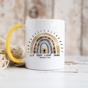 May include: White ceramic mug with a yellow handle. The mug features a watercolour rainbow with a cross in the centre and the text "Let your light shine Matthew 5:16".
