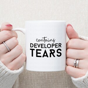 Peut inclure: Une tasse en c&eacute;ramique blanche avec du texte noir qui dit "contient des larmes de d&eacute;veloppeur".
