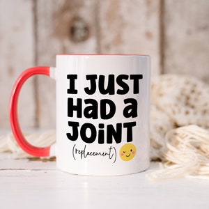 May include: A white ceramic mug with a bright red handle and interior rim. The front features bold black text that reads I JUST HAD A JOINT followed by the word (replacement) in a smaller script font and a small yellow smiling emoji face.