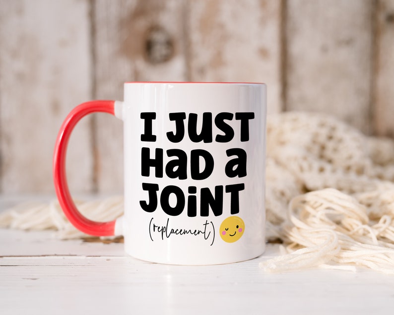 May include: A white ceramic mug with a bright red handle and interior rim. The front features bold black text that reads I JUST HAD A JOINT followed by the word (replacement) in a smaller script font and a small yellow smiling emoji face.