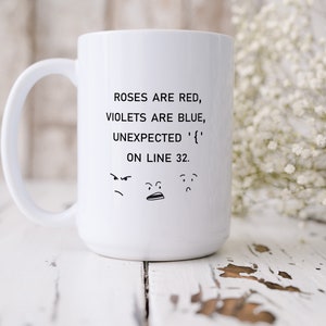 Może przedstawiać: Biały kubek ceramiczny z czarnym nadrukiem, na kt&oacute;rym widnieje napis "Roses are red, violets are blue, unexpected '{' on line 32." Pod tekstem znajdują się trzy kresk&oacute;wkowe twarze.