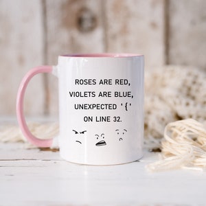 Może przedstawiać: Biały kubek ceramiczny z r&oacute;żowym rantem i uchwytem. Kubek zawiera humorystyczny cytat, kt&oacute;ry brzmi "Roses are red, violets are blue, unexpected '{' on line 32." z trzema kresk&oacute;wkowymi twarzami pod tekstem.