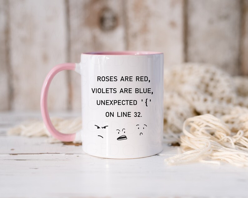 Może przedstawiać: Biały kubek ceramiczny z r&oacute;żowym rantem i uchwytem. Kubek zawiera humorystyczny cytat, kt&oacute;ry brzmi "Roses are red, violets are blue, unexpected '{' on line 32." z trzema kresk&oacute;wkowymi twarzami pod tekstem.