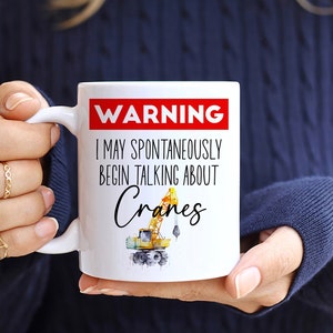 May include: White ceramic mug with a red warning sign that says "WARNING I MAY SPONTANEOUSLY BEGIN TALKING ABOUT Cranes". A yellow crane illustration is below the text.