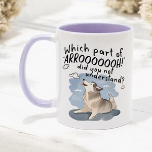 May include: A white ceramic mug with a light purple interior and handle. The front features a cartoon illustration of a howling husky dog and the black text: Which part of 'ARROOOOOOH!' did you not understand? The design includes small cloud accents.