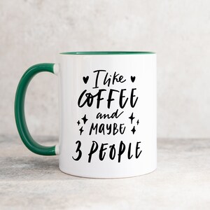 May include: White coffee mug with a green rim and handle. The mug has black text that reads "I like coffee and maybe 3 people" with hearts and stars around the text.
