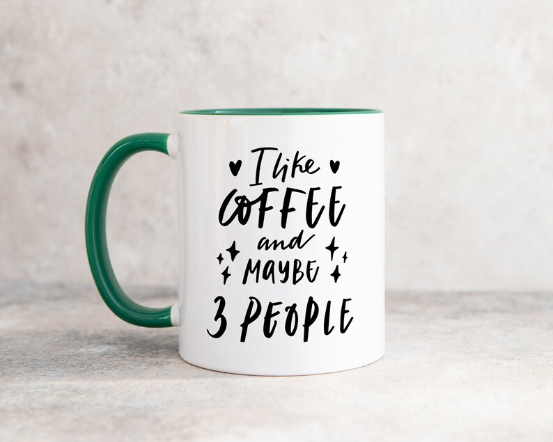 May include: White coffee mug with a green rim and handle. The mug has black text that reads "I like coffee and maybe 3 people" with hearts and stars around the text.