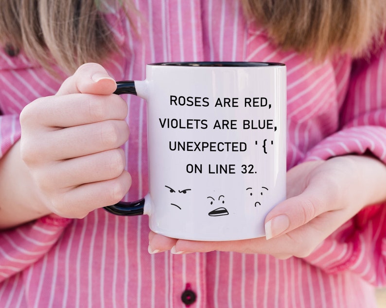 Może przedstawiać: Biały kubek ceramiczny z czarnym uchwytem i rantem. Kubek ma humorystyczny napis: "Roses are red, violets are blue, unexpected '{' on line 32." Kubek ma r&oacute;wnież trzy kresk&oacute;wkowe twarze na dole.