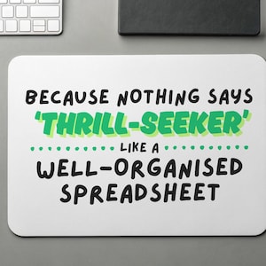 Può includere: Un tappetino per mouse bianco con la scritta "BECAUSE NOTHING SAYS 'THRILL-SEEKER' LIKE A WELL-ORGANISED SPREADSHEET" in nero e verde. Sono visibili anche un mouse bianco, una tastiera, una matita e un blocco note.