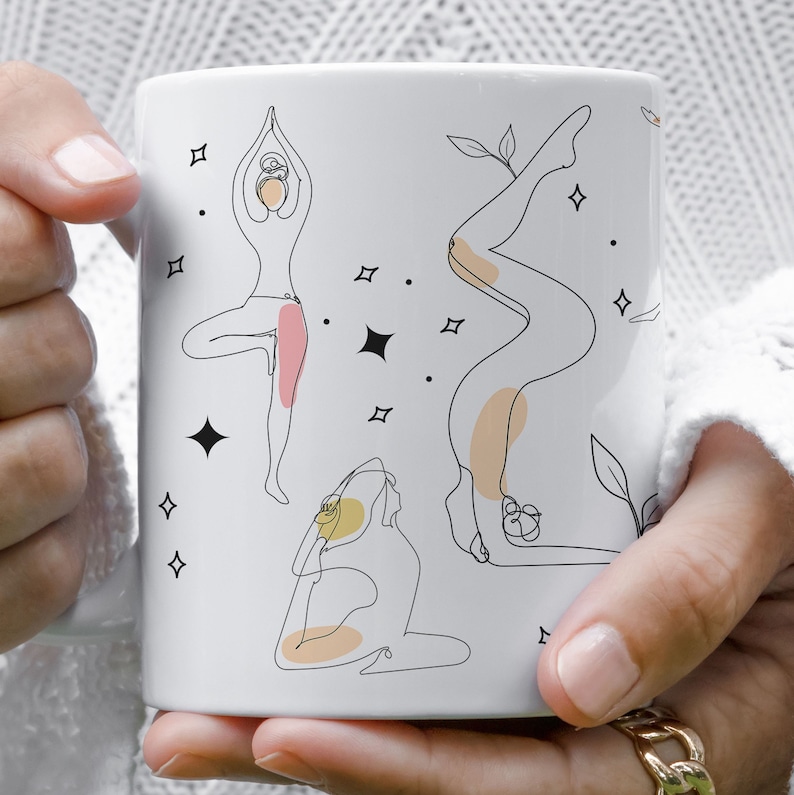 May include: White ceramic mug with black line art illustrations of yoga poses, accented with peach and yellow. The design includes stars and leaves. The mug is held by a person.