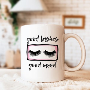 May include: White ceramic coffee mug with black text that reads "good lashes good mood". The mug has a pink and black illustration of a pair of eyelashes.