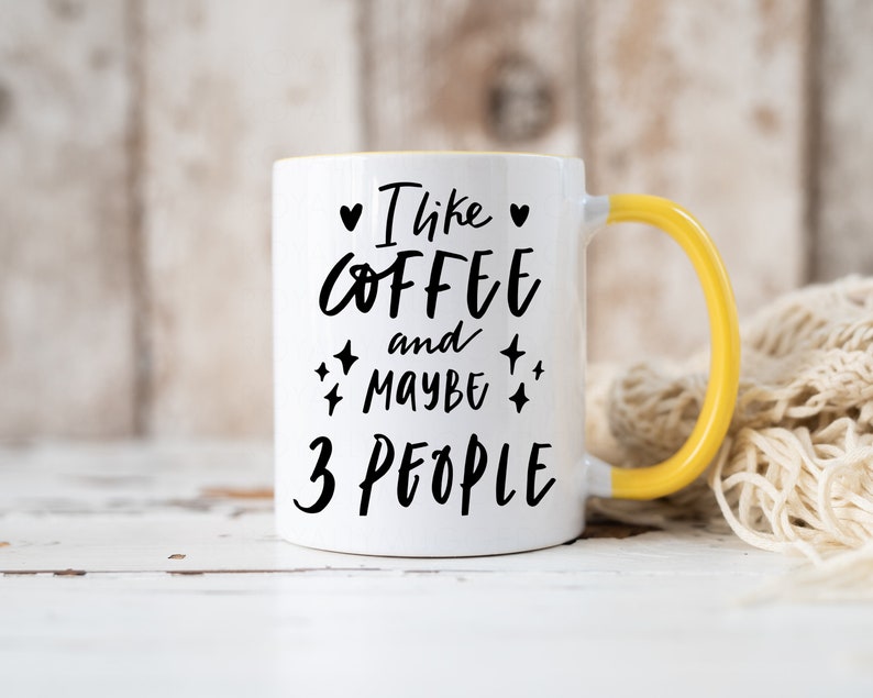 May include: White ceramic mug with a yellow handle. The mug has black text that reads "I like coffee and maybe 3 people" with a heart and stars around the text.