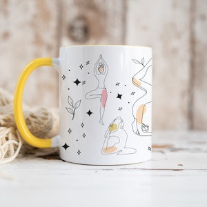 May include: White ceramic mug with a yellow handle and interior. The mug features line art illustrations of yoga poses, with accents of pink and yellow. Black star and leaf designs are also present.