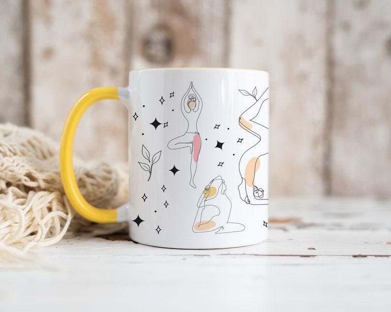 May include: White ceramic mug with a yellow handle and interior. The mug features line art illustrations of yoga poses, with accents of pink and yellow. Black star and leaf designs are also present.