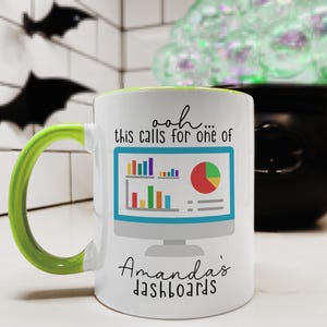 May include: A white ceramic mug with a bright lime green handle and interior. The front features a graphic of a computer monitor displaying colorful bar and pie charts, with the text "ooh... this calls for one of Amanda's dashboards" printed in black.