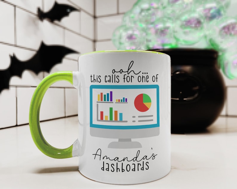 May include: A white ceramic mug with a bright lime green handle and interior. The front features a graphic of a computer monitor displaying colorful bar and pie charts, with the text "ooh... this calls for one of Amanda's dashboards" printed in black.