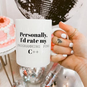 May include: White ceramic mug with black text that reads "Personally, I'd rate my programming puns C++".
