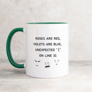 Może przedstawiać: Biały kubek do kawy z zielonym rantem i uchwytem. Kubek ma humorystyczny napis: "Roses are red, violets are blue, unexpected '{' on line 32." z trzema kresk&oacute;wkowymi twarzami pod tekstem.