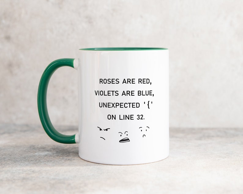 Może przedstawiać: Biały kubek do kawy z zielonym rantem i uchwytem. Kubek ma humorystyczny napis: "Roses are red, violets are blue, unexpected '{' on line 32." z trzema kresk&oacute;wkowymi twarzami pod tekstem.