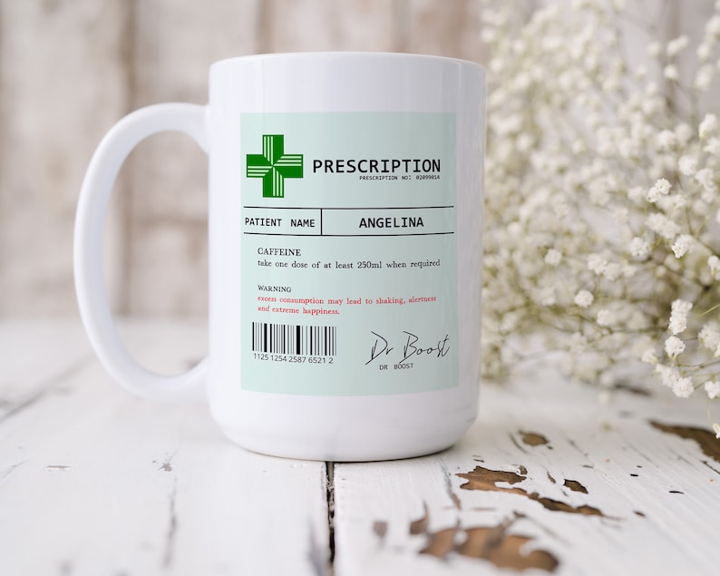 May include: White ceramic mug with a green cross and the text "PRESCRIPTION" and "ANGELINA". The mug has a black barcode and the text "CAFFEINE" and "take one dose of at least 250ml when required".