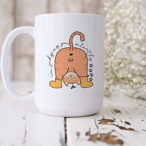May include: White ceramic coffee mug with a cartoon orange cat wearing yellow boots and the text "I'm judging you silently" in black cursive.