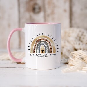 May include: White ceramic mug with a pink handle. The mug features a watercolour rainbow with a cross in the centre and the text "Let your light shine Matthew 5:16".