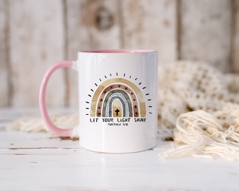 May include: White ceramic mug with a pink handle. The mug features a watercolour rainbow with a cross in the centre and the text "Let your light shine Matthew 5:16".