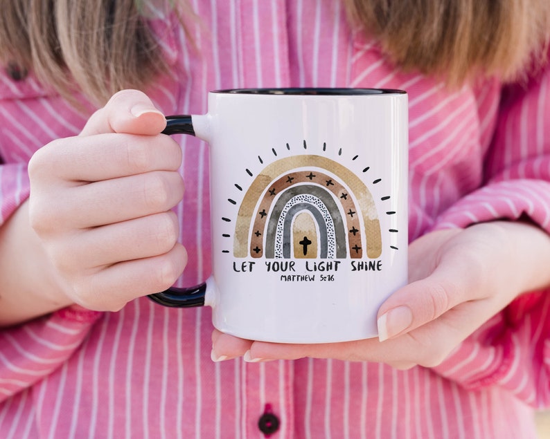 May include: White ceramic mug with a black handle. The mug features a watercolour rainbow with a cross in the centre and the text "Let your light shine Matthew 5:16".